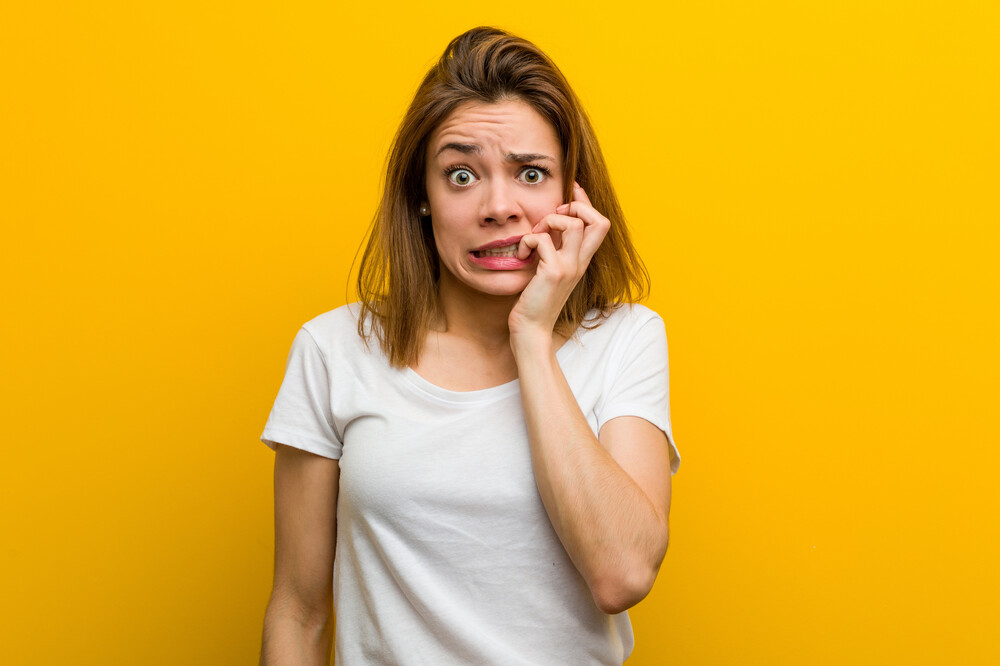 Young natural caucasian woman biting fingernails, nervous and very anxious.